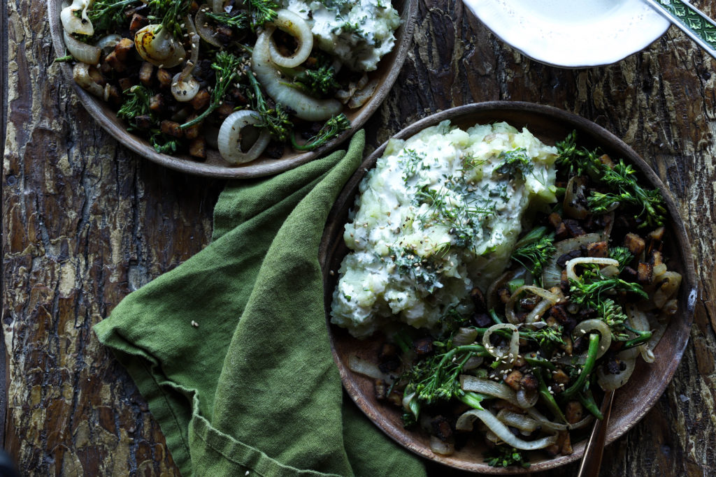 bowls of mashed potatoes, caramelized onions, and tempeh with green napkin and wood background