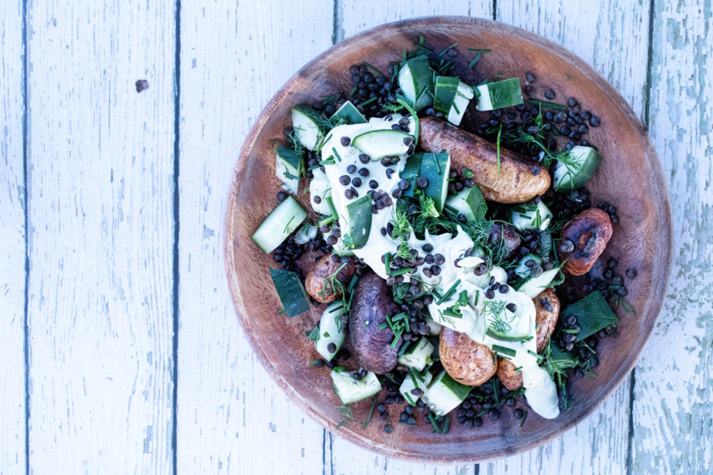 a wooden plate with crispy roast potatoes and cucumber lentil salad with lemon dill hummus