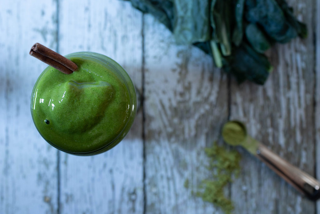 a creamy matcha shake is shown along with matcha powder, kale, and cinnamon