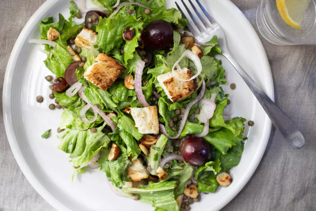 Salad with croutons, shallots, and lentils on a white plate with a fork