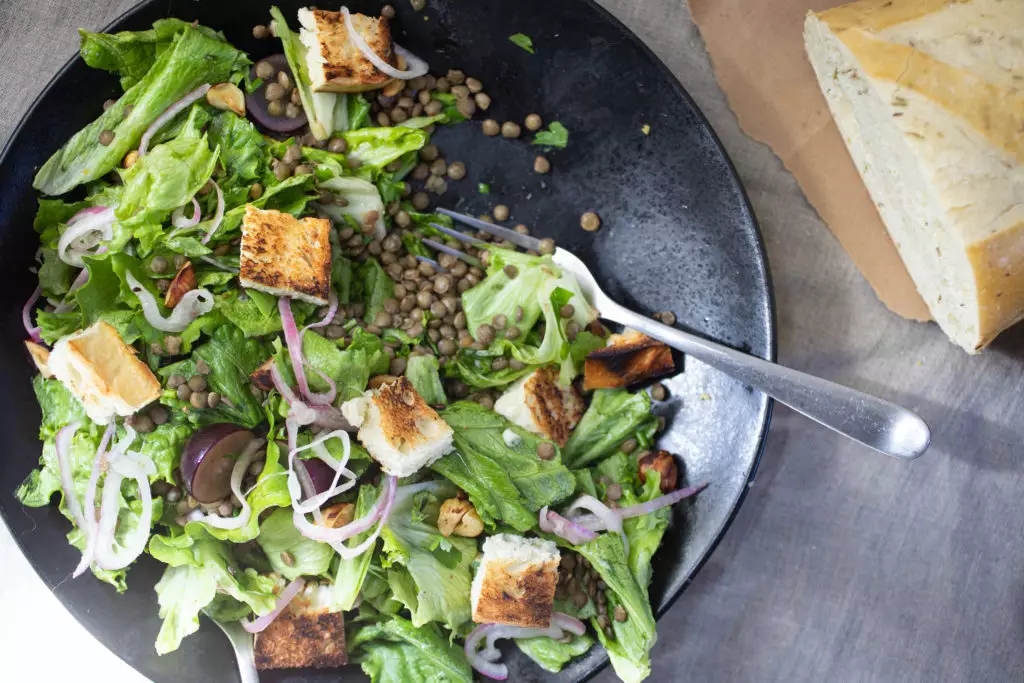 salad on a black plate with croutons and lentils