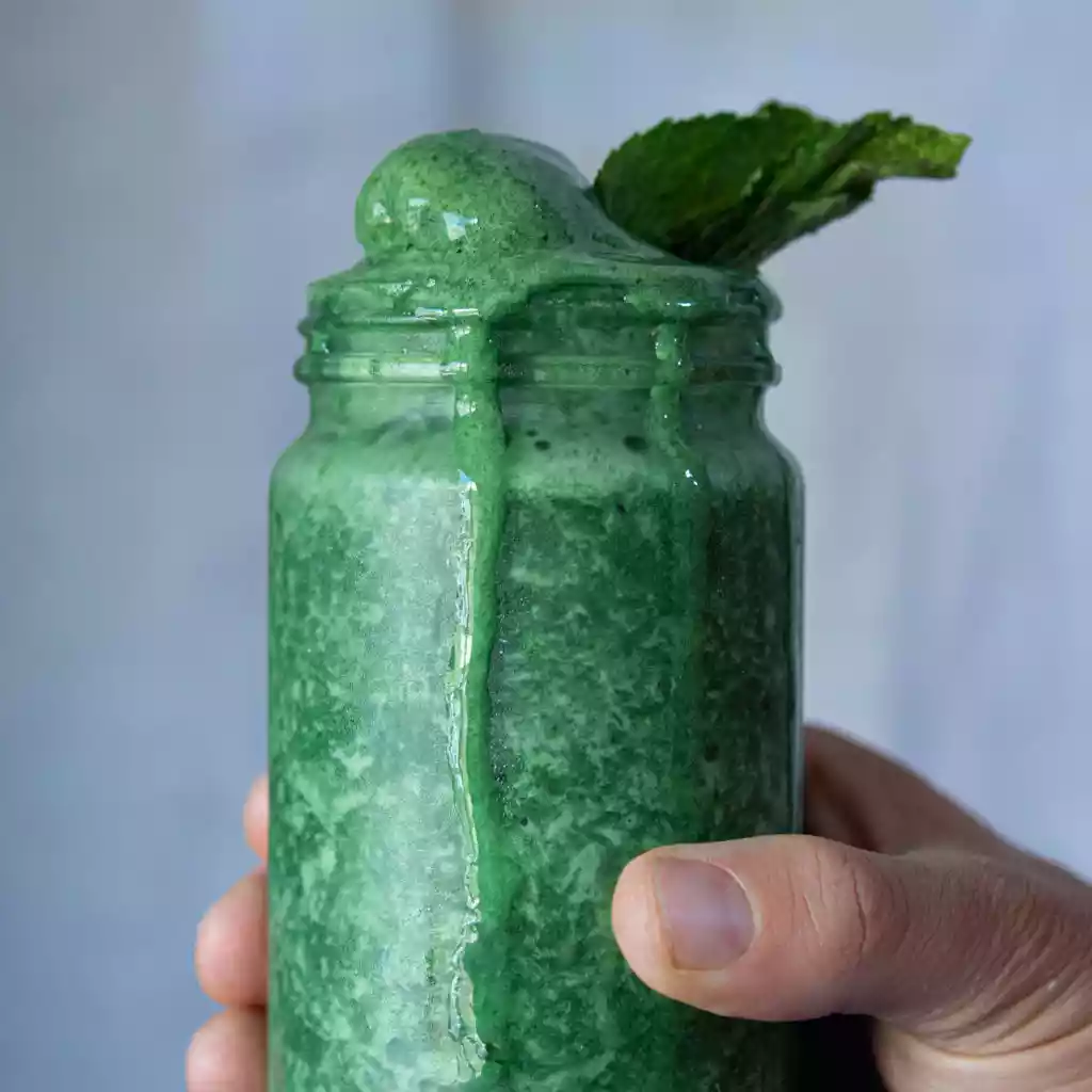 A close up, handheld shot of a vibrant green smoothie garnished with mint leaves