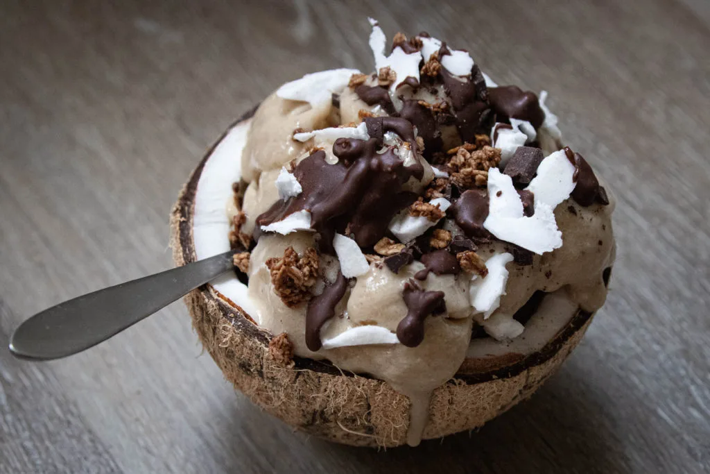 smoothie in a halved coconut drizzled with chocolate and topped with coconut shavings and granola