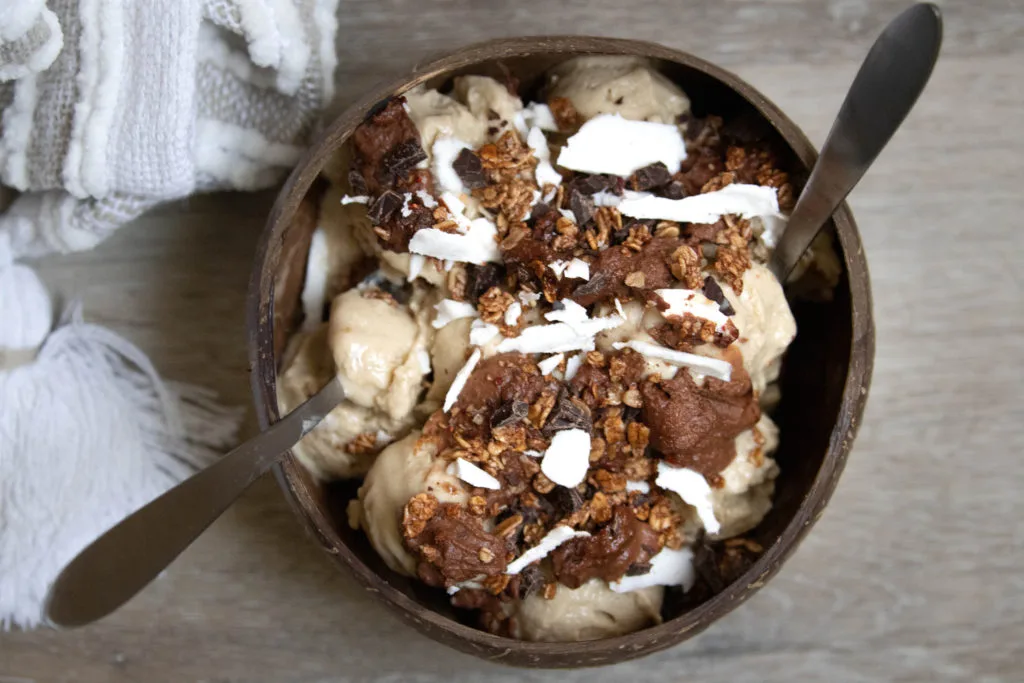 A coconut smoothie topped with chocolate peanut butter sauce, flaked coconut meat, and chocolate granola