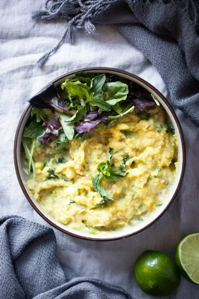 a bowl of golden stew with fresh leaves garnished with lime