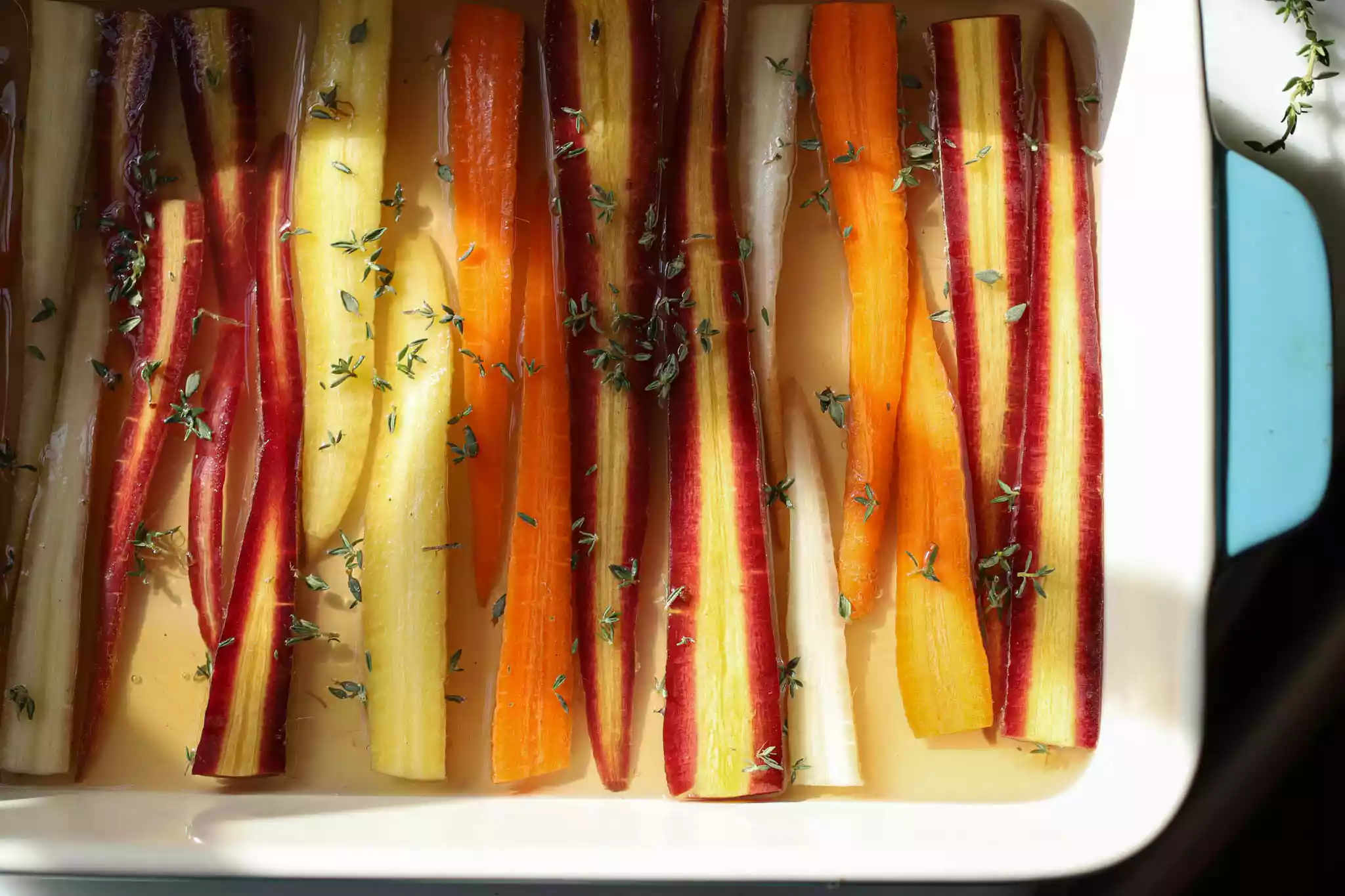 halved, colorful carrots are arranged on a blue baking dish and sprinkled with thyme