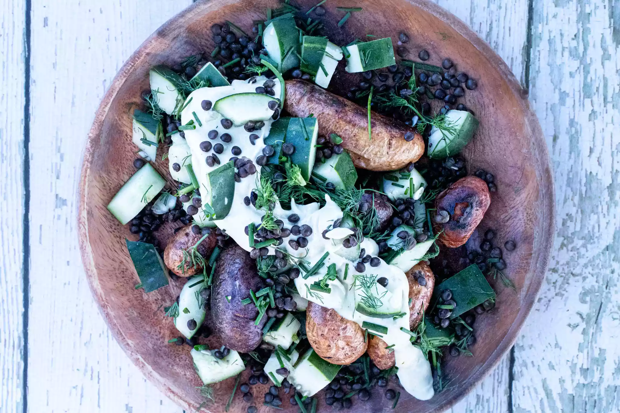 a wooden plate with crispy roast potatoes and cucumber lentil salad with lemon dill hummus