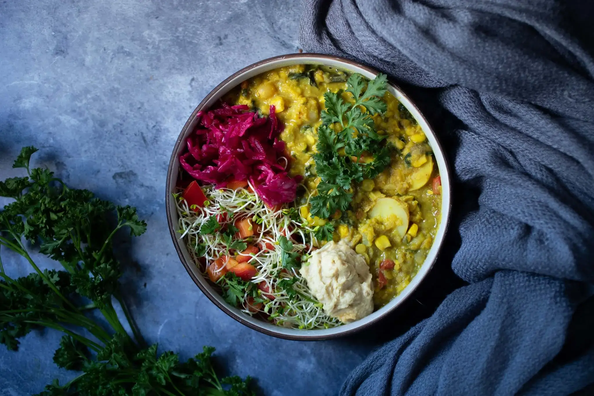 a bowl of golden lentils with purple sauerkraut on a blue table